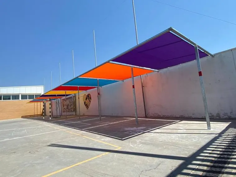 Toldos de lona morada, naranja, roja y azul sobre la pista deportiva del CEIP Nebrixa de Lebrija