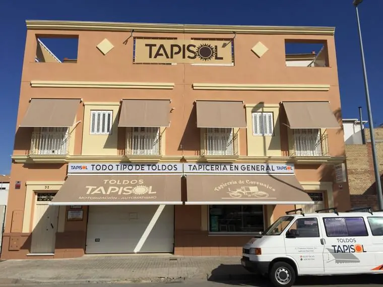 Fachada del taller de Tapisol en la calle Dámaso Alonso de Lebrija, con toldos en todas las ventanas